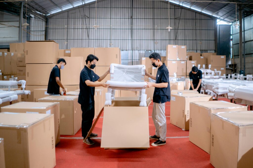 Men in a warehouse wearing masks, assembling and packing furniture into boxes with efficiency.
